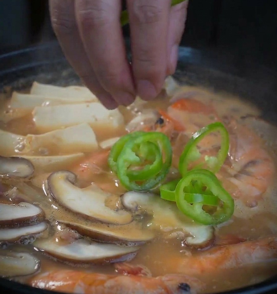 Anelli di peperone verde che vengono fatti cadere a mano nella zuppa di pasta di soia e pesce.