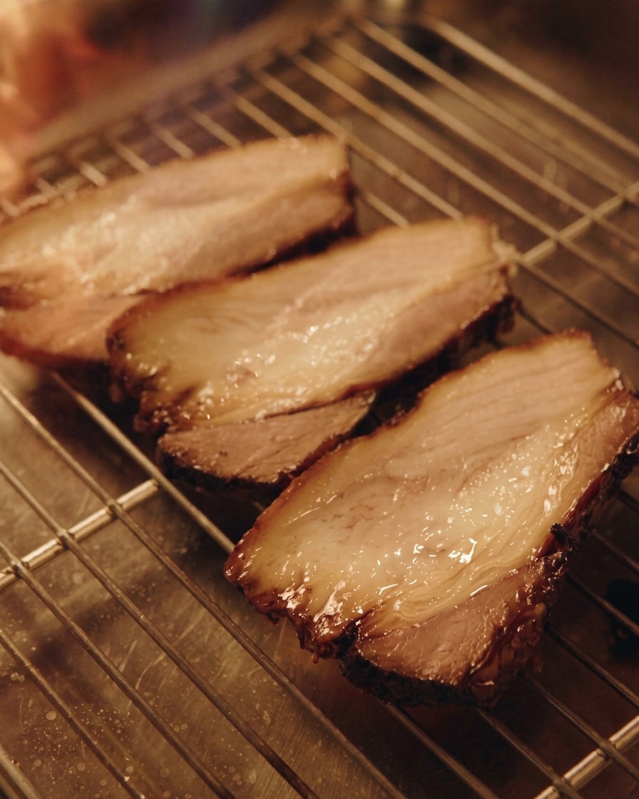 Un cannello da cucina che scotta tre spesse fette di maiale chashu appoggiate su una griglia metallica.