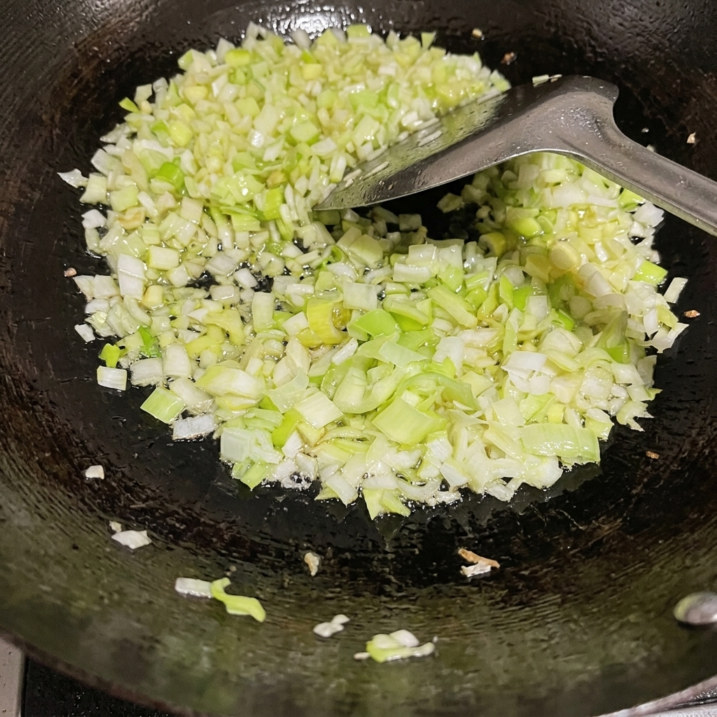 Cipollotti tritati finemente saltati in un wok nero condito con olio e una spatola di metallo.