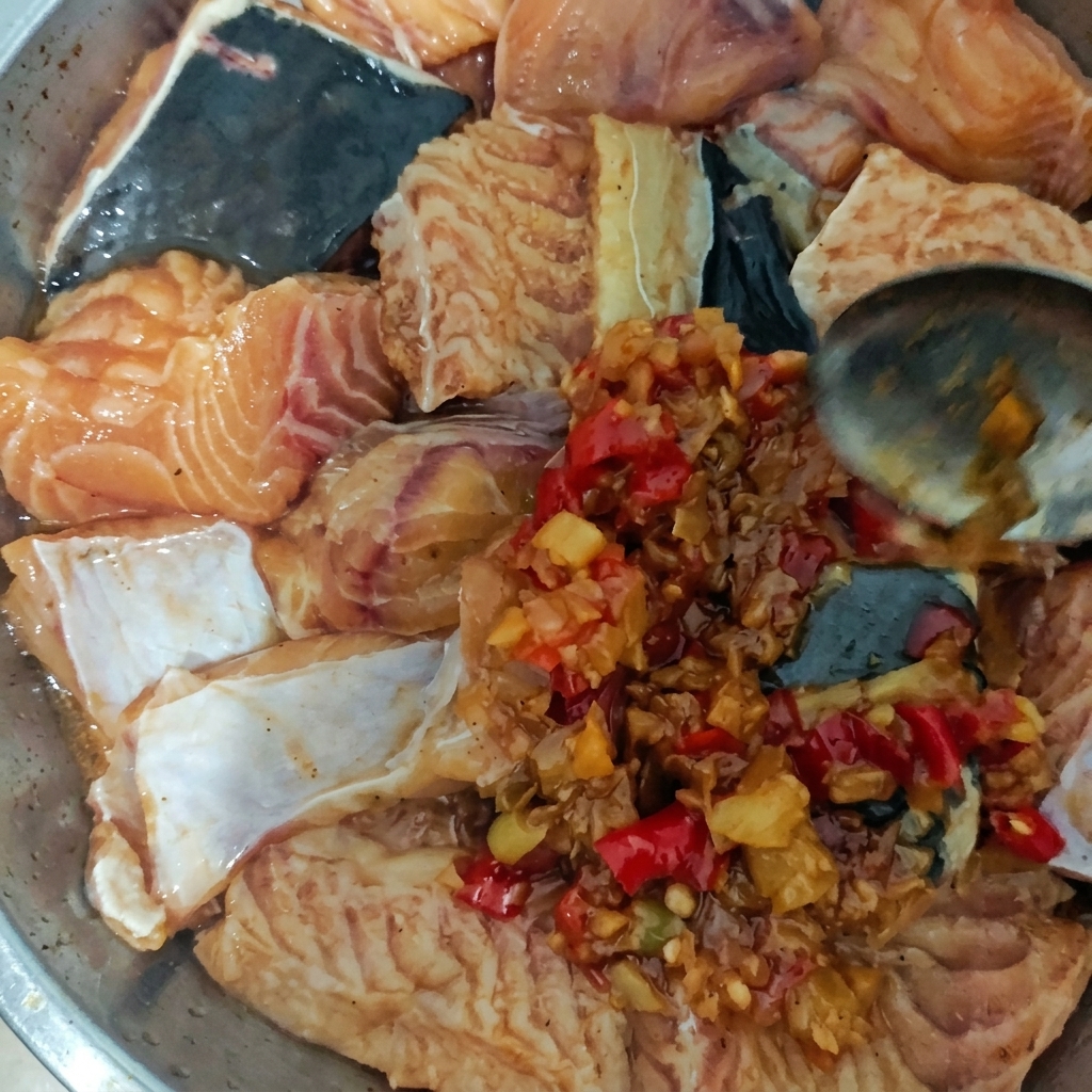 Un piatto di metallo pieno di pezzi di pesce crudo conditi con una densa salsa di peperoncini rossi e aglio usando un cucchiaio.