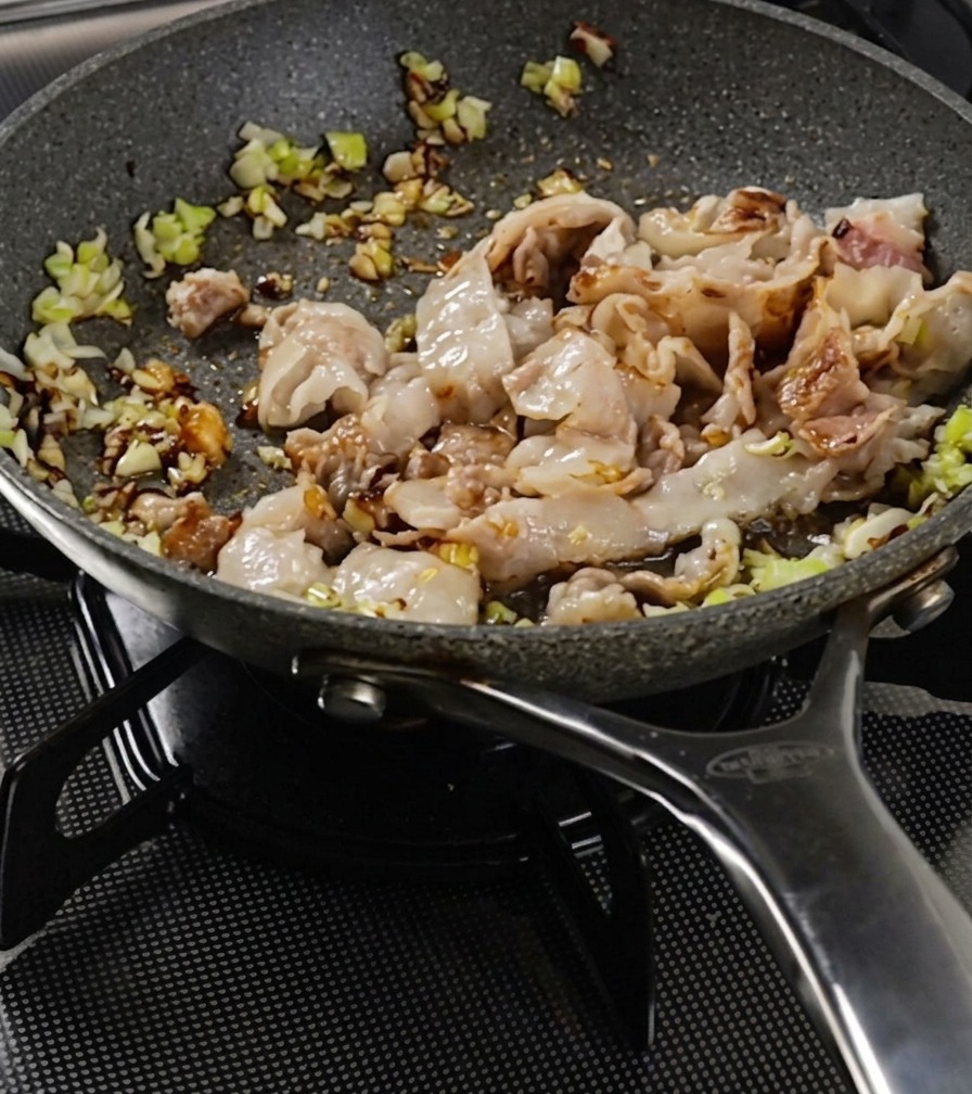 Strisce di pancetta di maiale e cipollotti saltati in padella finché la superficie della carne non appare ben dorata.