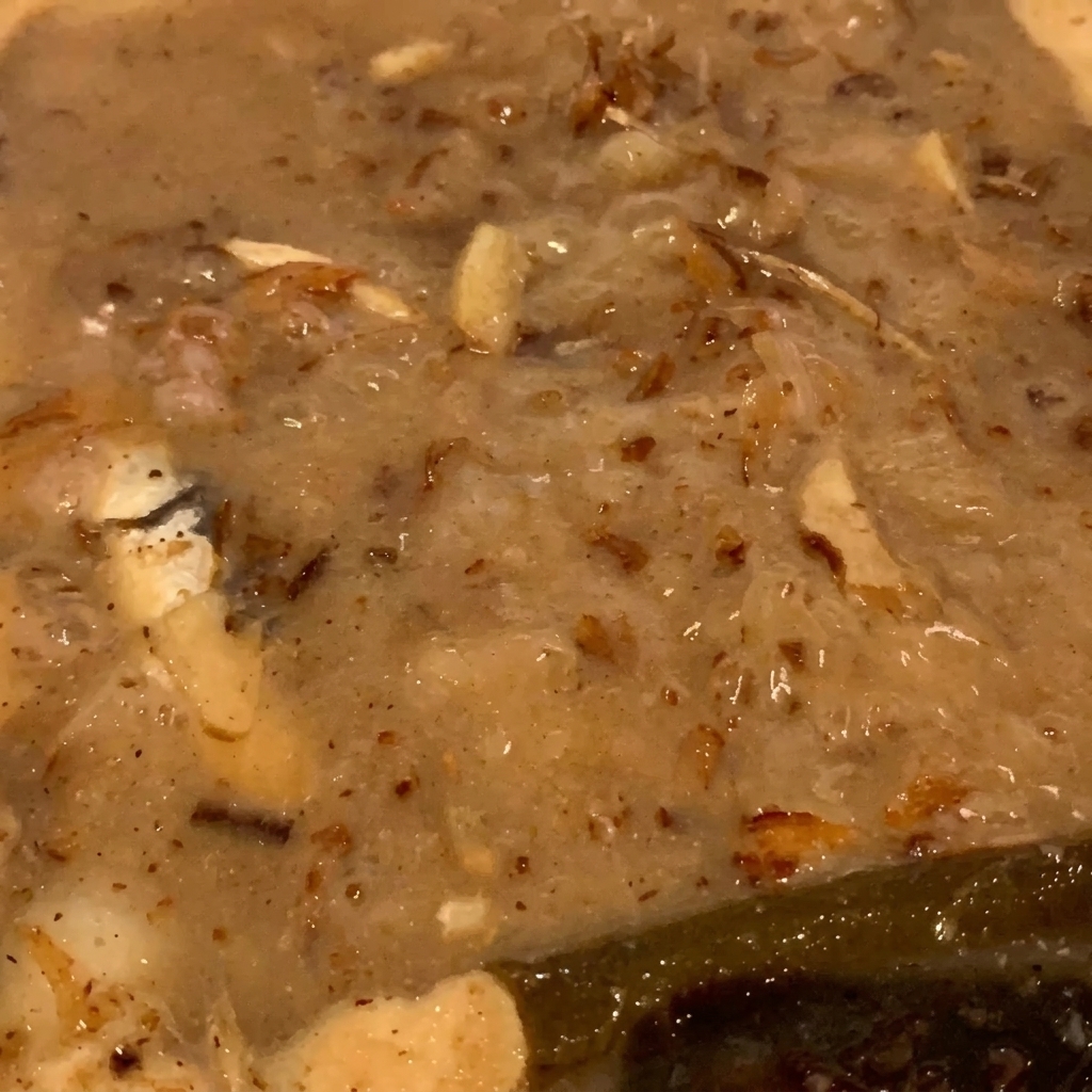 Un primo piano di scaglie di pesce e piccoli pesci che sobbollono in un liquido denso color nocciola.