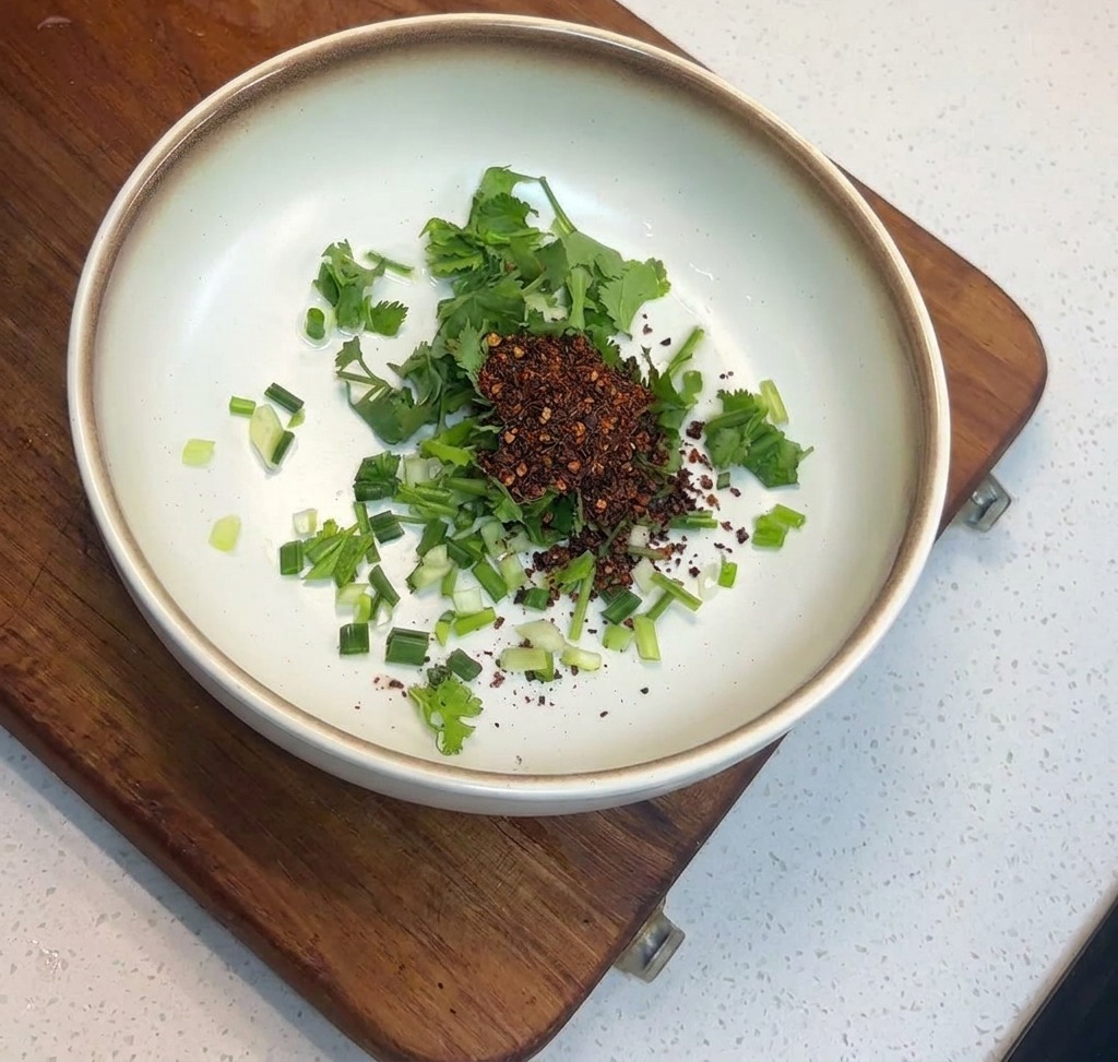 Una montagna di fiocchi di peperoncino rosso scuro sopra erbe verdi in una ciotola di ceramica.