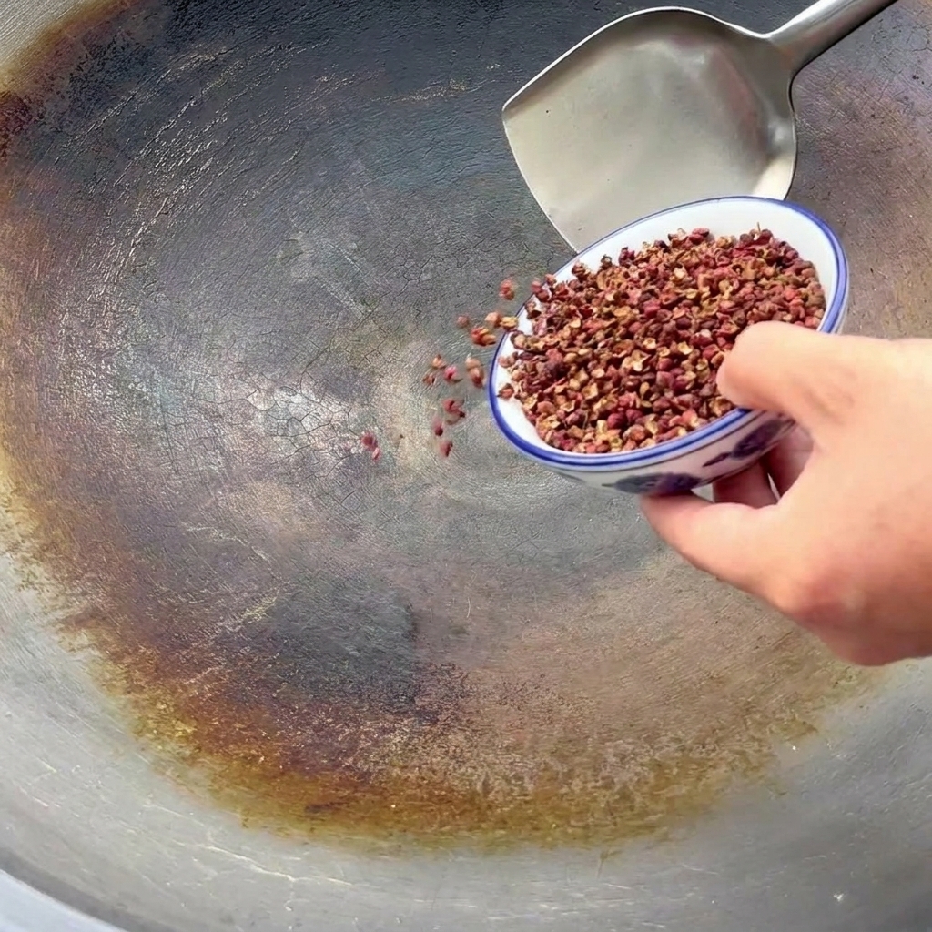 Pepe di Sichuan versato da una ciotolina in un grande wok per la tostatura.