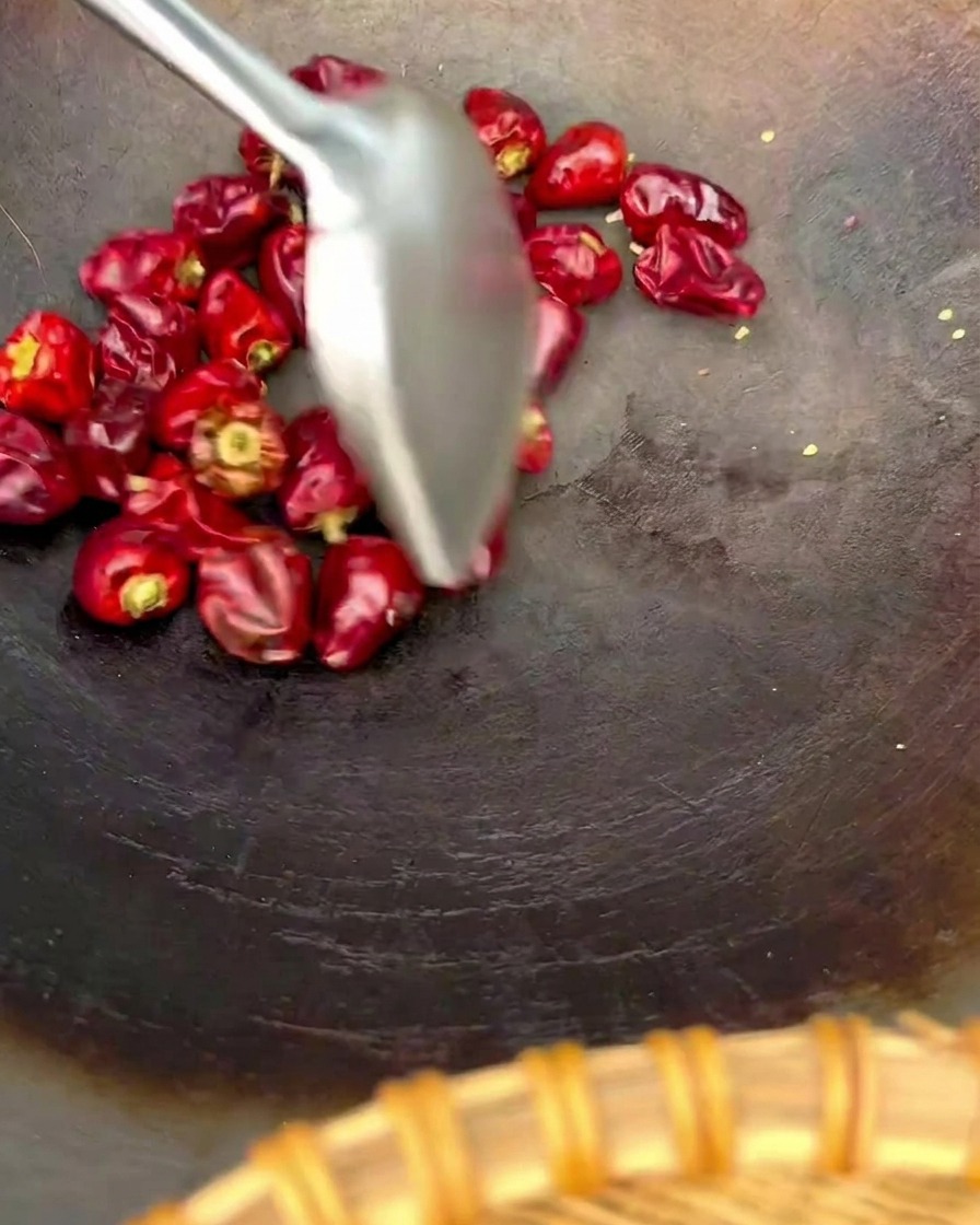 Spatola di metallo che mescola una manciata di peperoncini lanterna rossi e tondi in un wok.