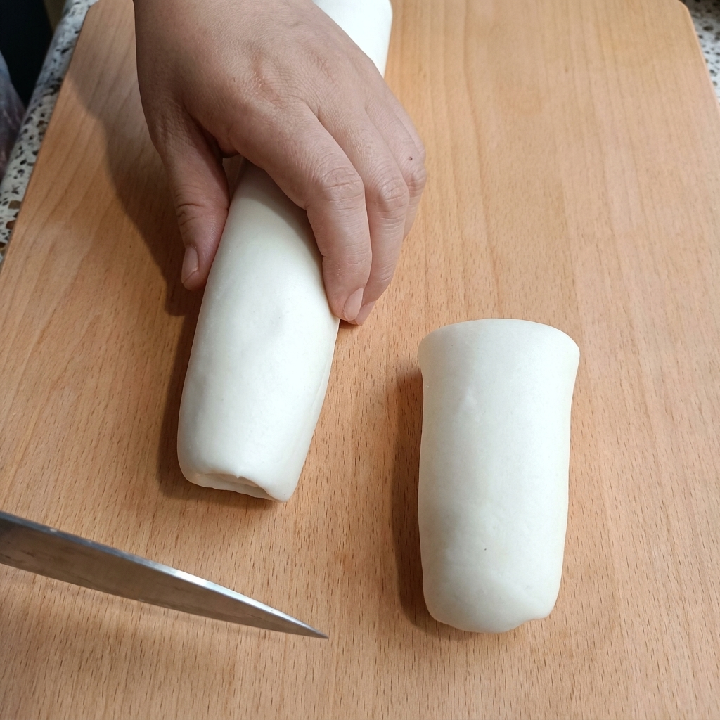 Una mano che tiene un cilindro di pasta bianca su un tagliere mentre lo taglia con un coltello.