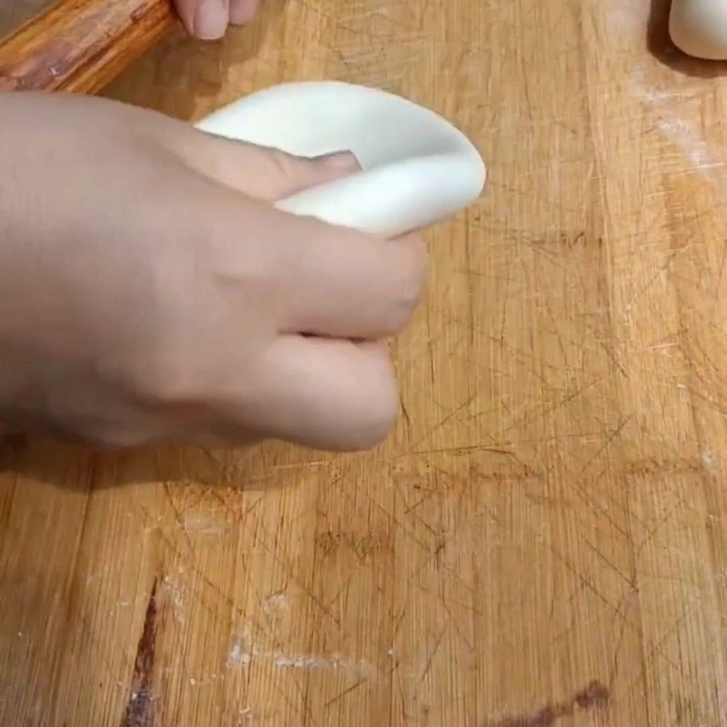 Una mano che usa un mattarello di legno per appiattire un pezzo di pasta in un disco spesso su un tagliere.