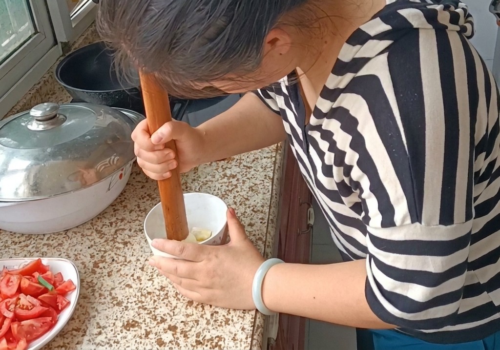 Una persona che usa un pestello di legno per schiacciare spicchi daglio in una pasta fine in una ciotolina.