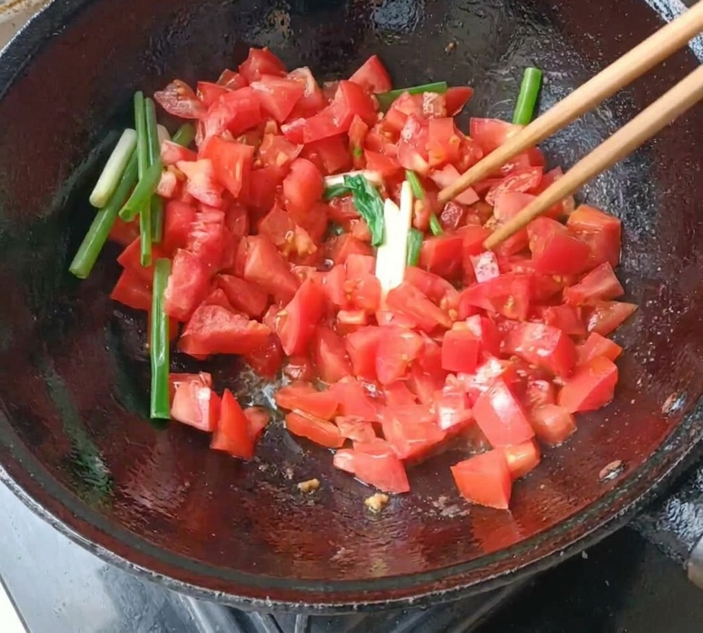 Pomodori a dadini e segmenti di cipollotto saltati in un wok con bacchette di legno.