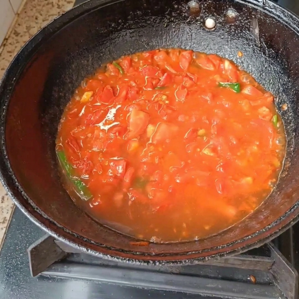 Pomodori e cipollotti che sobbollono in acqua allinterno di un wok nero su un fornello a gas.