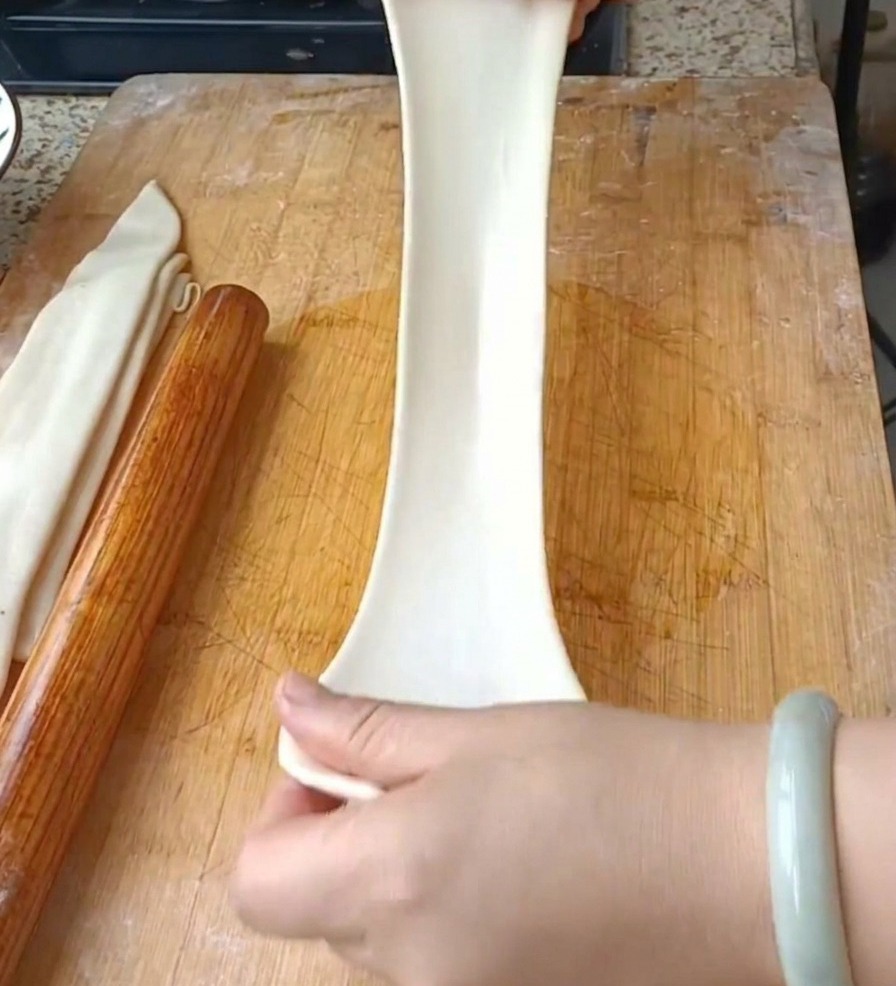 Due mani che tirano verticalmente una striscia di pasta larga e traslucida per formare un lungo spaghetto piatto.