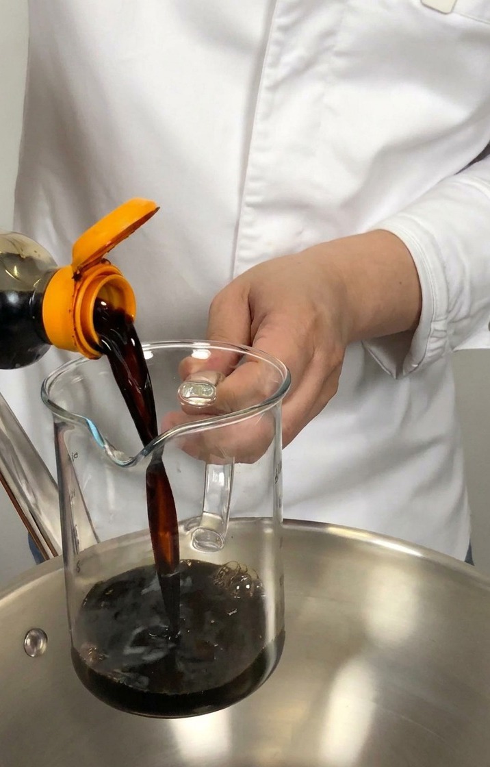 Salsa di soia giapponese versata in un misurino di vetro sopra un pentolino in acciaio.
