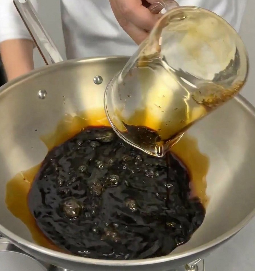 Versamento di mirin trasparente in una pentola che già contiene la salsa di soia scura.