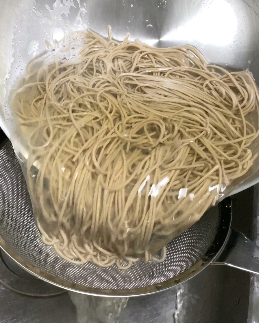 Tagliolini di soba cotti versati in un colino nel lavandino per eliminare lacqua bollente.
