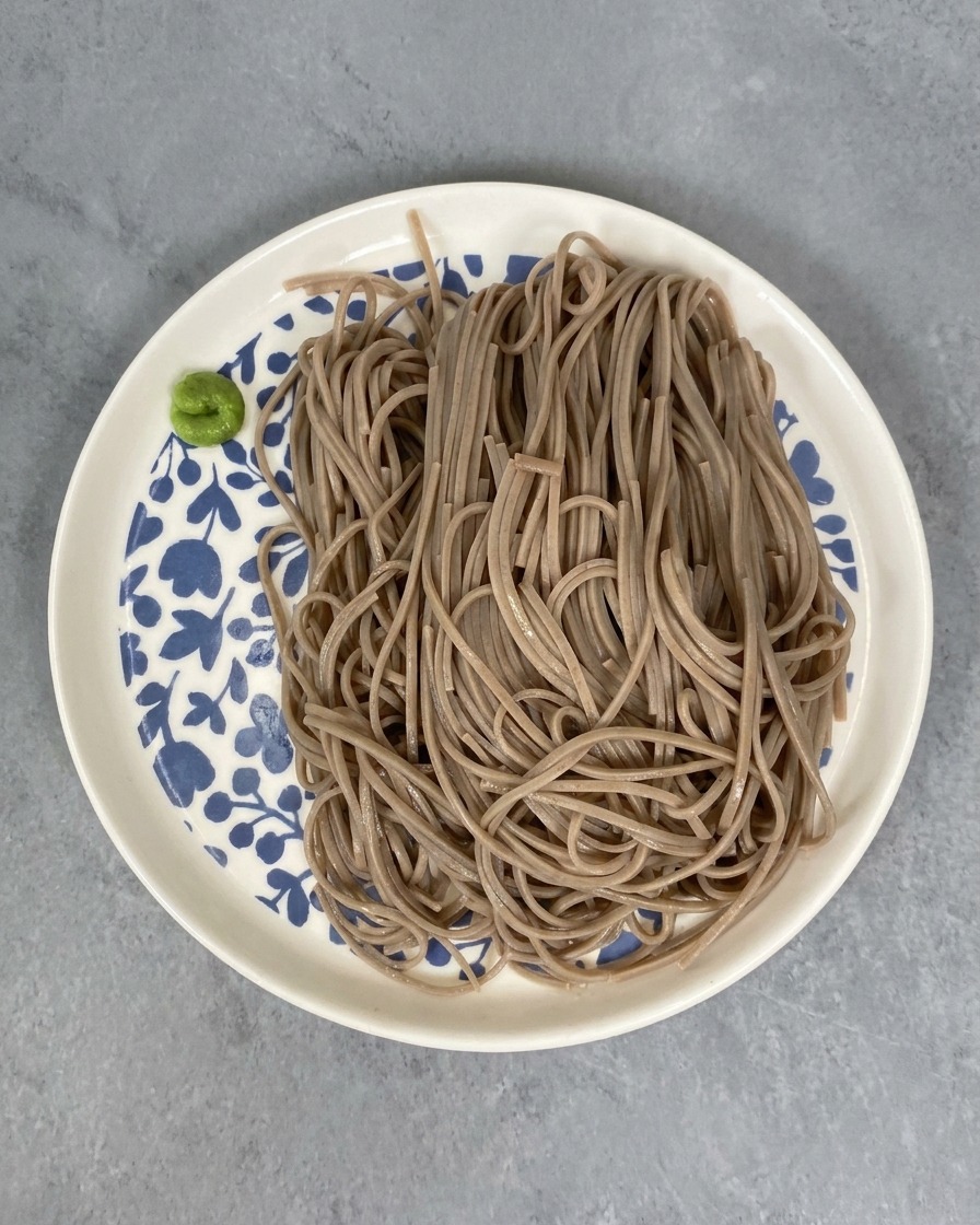 Porzione di soba su un piatto decorato con una piccola quantità di pasta wasabi verde sul lato.