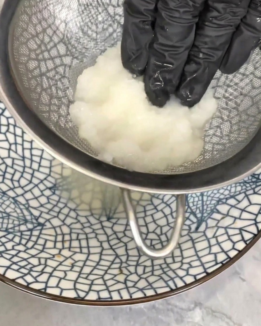 Mano che preme la polpa di daikon grattugiato in un colino per eliminare il liquido in eccesso.