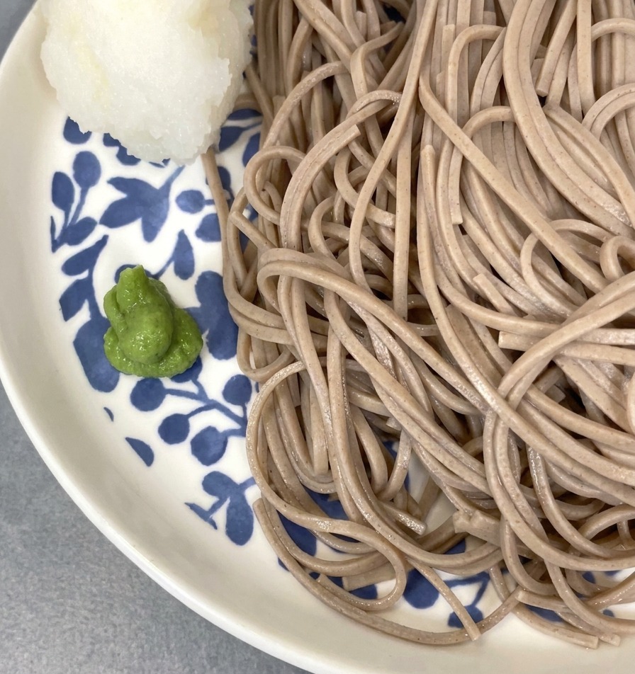 Soba fredda servita su un piatto fiorito, guarnita con una pallina di daikon e una punta di wasabi.