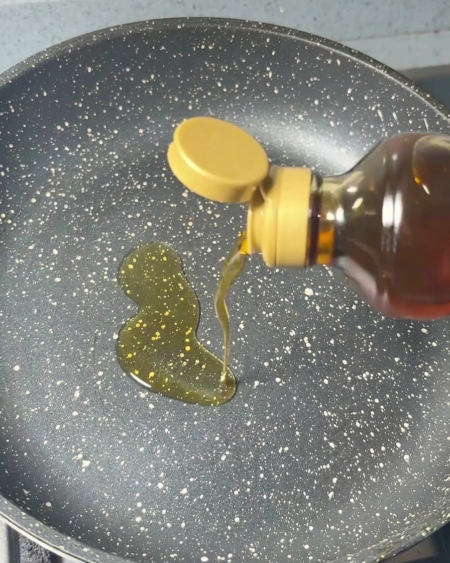 Olio di sesamo versato in una padella scura con un movimento circolare costante.