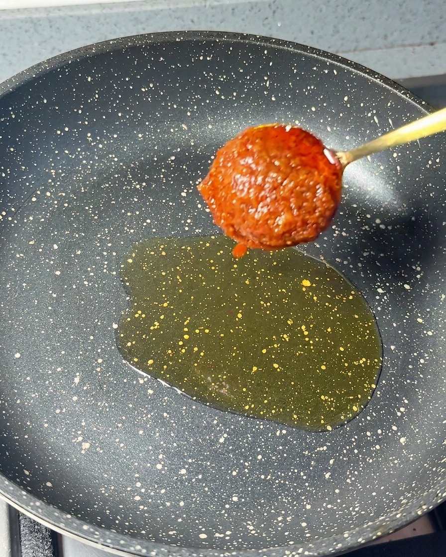 Un cucchiaio di densa pasta di gamberi rossa aggiunto in padella con lolio di sesamo.