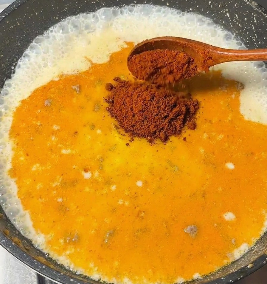 Un cucchiaio di legno che aggiunge pezzi di curry roux in una salsa a base di latte che sobbolle.