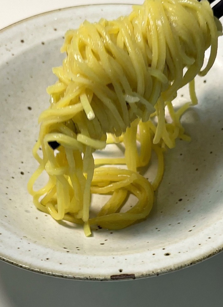 Noodles gialli cotti sollevati con le bacchette e adagiati in una ciotola di ceramica chiara.