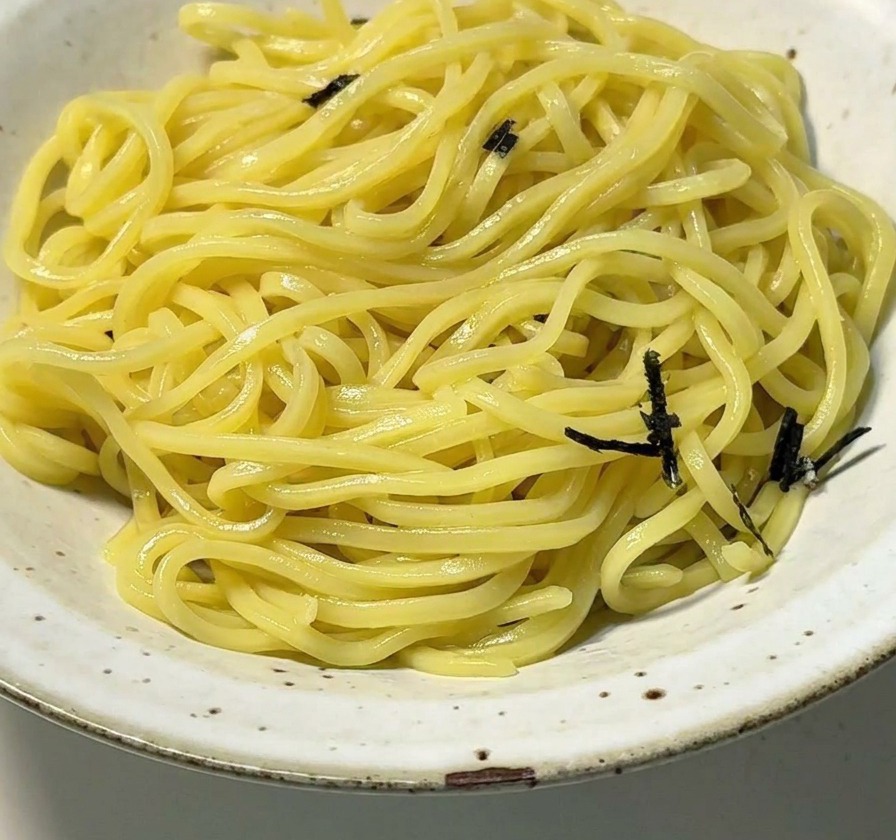 Ciotola in ceramica con noodles gialli sormontati da striscioline di alga nori nera.