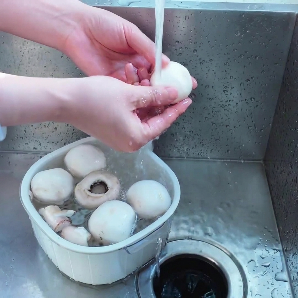 Una persona che lava diversi funghi champignon bianchi interi in un piccolo colino di plastica bianca sotto lacqua corrente.