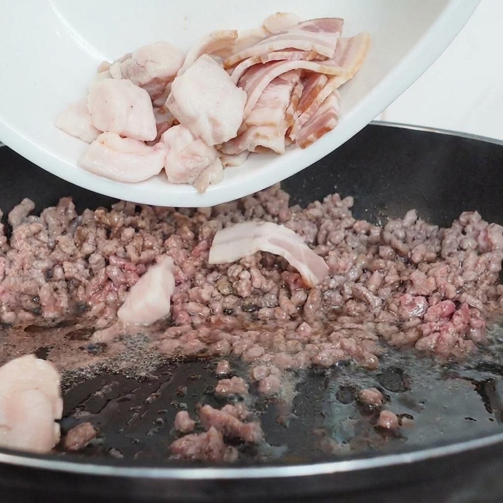 Funghi bianchi affettati versati da un piatto bianco in una padella nera contenente carne macinata parzialmente cotta.