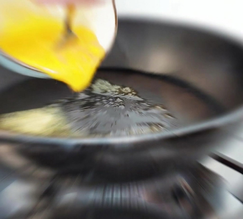 Uovo liquido sbattuto versato da una ciotola in una padella calda con burro fuso.