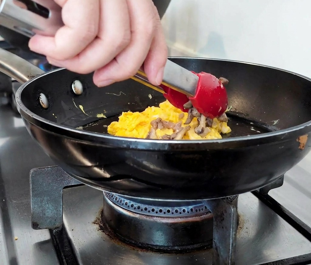 Carne macinata cotta e funghi affettati ammucchiati su un letto di uova strapazzate soffici in padella.
