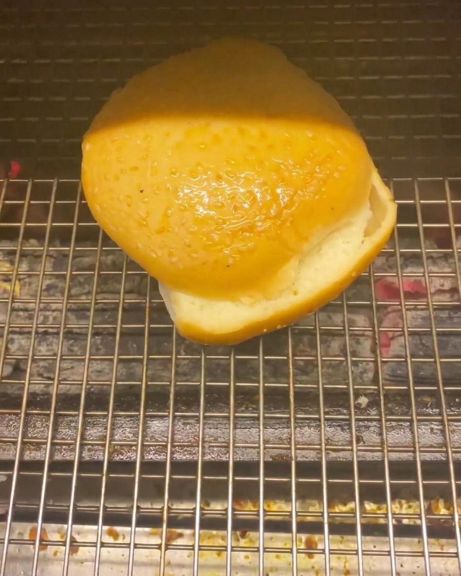 Un panino per hamburger sulla griglia sopra i carboni ardenti per la tostatura.