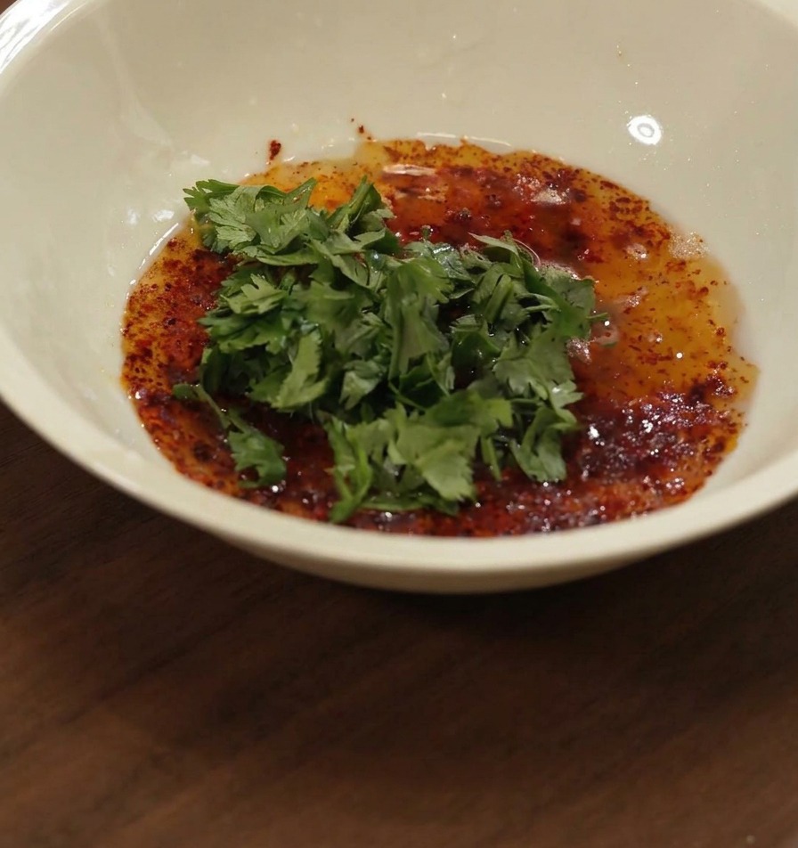 Miele versato in una ciotola bianca contenente una miscela di olio rosso, spezie e coriandolo verde tritato.
