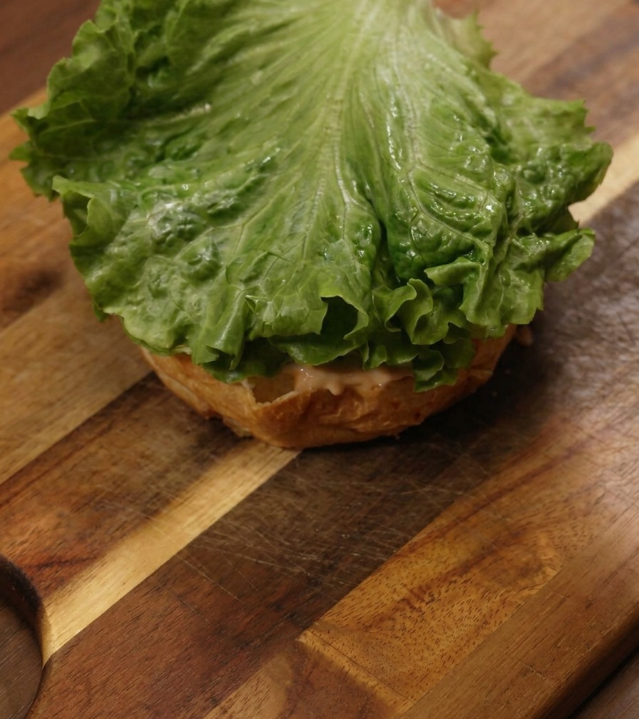 Una foglia di lattuga verde brillante appoggiata sopra un panino condito su un tagliere di legno.