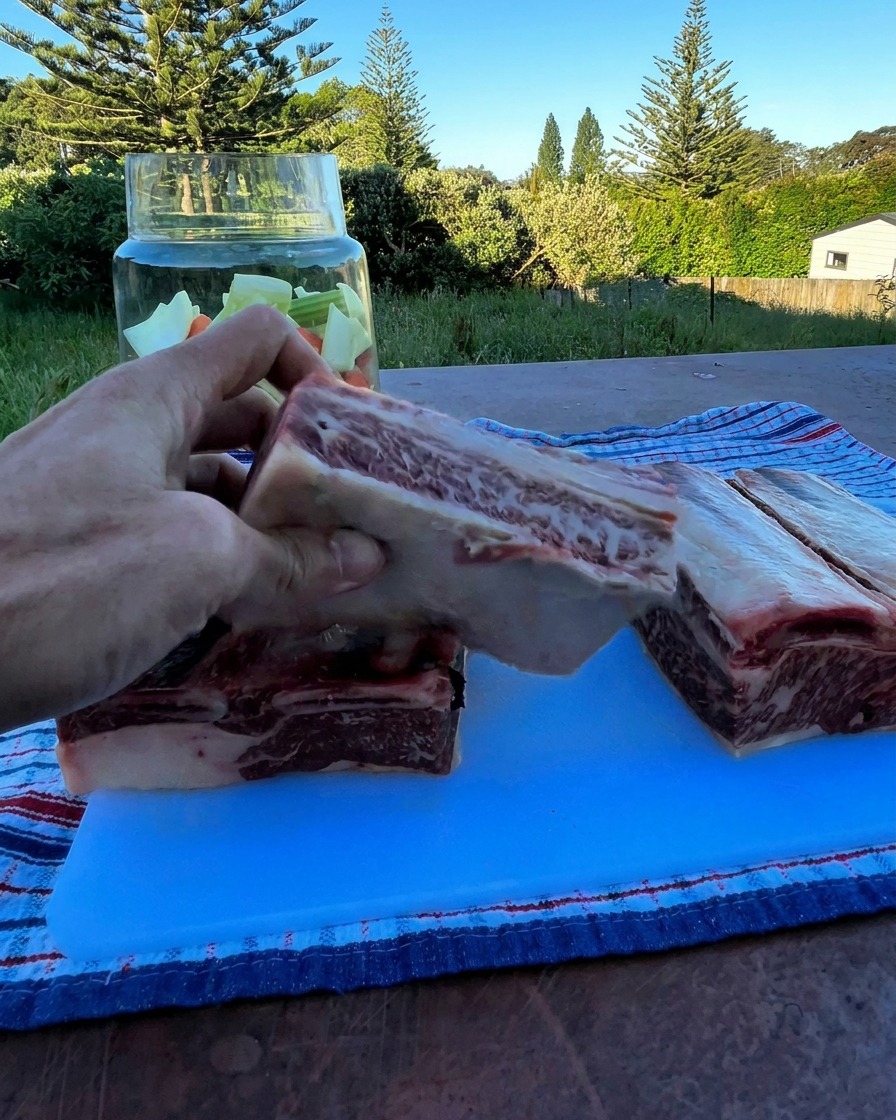 Una mano tiene una spessa costina di manzo cruda sopra un contenitore di vetro pieno di verdure tritate.