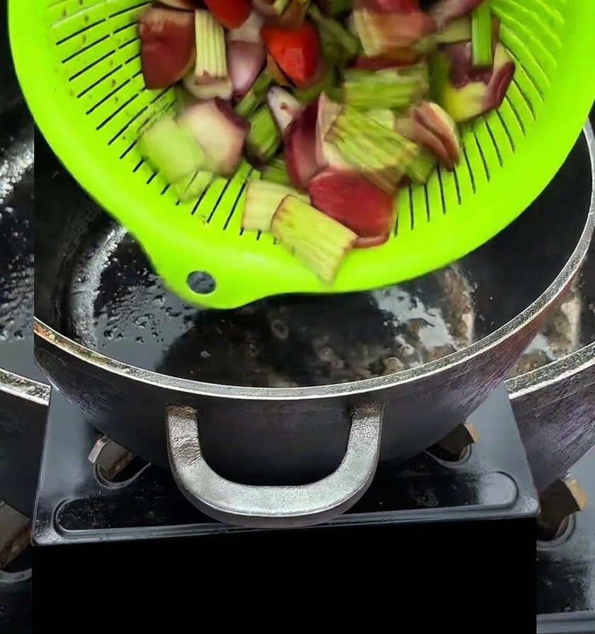 Verdure tritate versate da uno scolapasta verde brillante in una pentola nera calda.