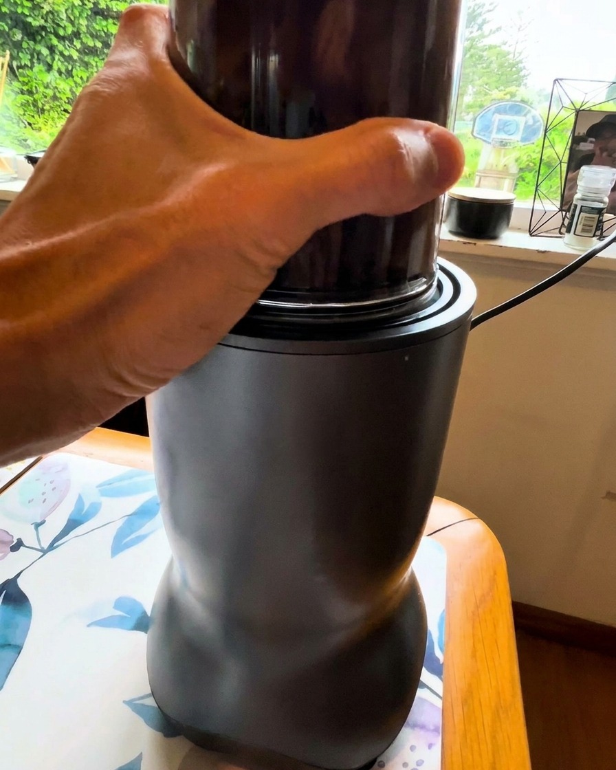 Una mano tiene il bicchiere di un piccolo frullatore mentre riduce in crema un composto scuro di verdure.
