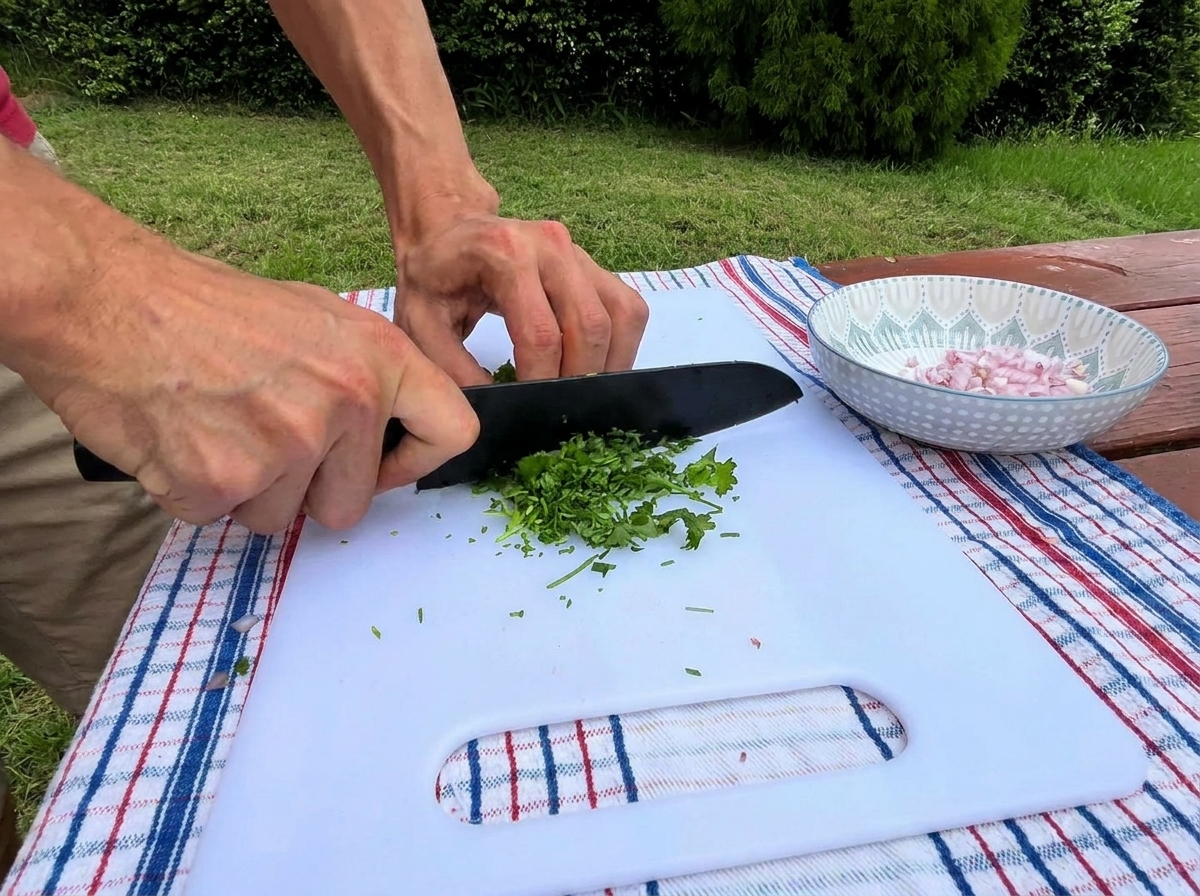 Mani di una persona utilizzano un coltello nero per tritare finemente del prezzemolo verde fresco su un tagliere bianco accanto a una ciotolina di scalogno a cubetti.