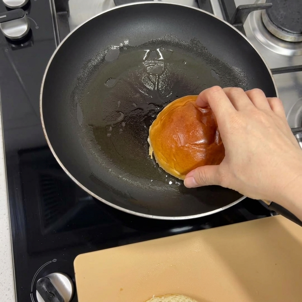 Una mano che mette un panino brioche in una padella calda per tostarlo fino a doratura.