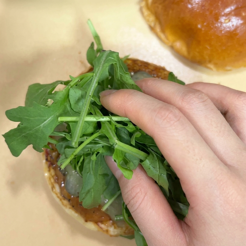 Una mano che mette un mazzetto di rucola fresca sopra i cetriolini in un panino da burger.