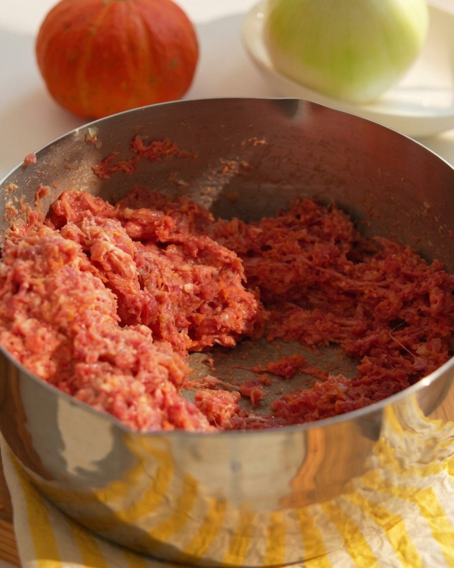 Una ciotola di metallo riempita con un mix di carne macinata di manzo cruda, cipolle tritate e ingredienti leganti preparati per formare gli hamburger.