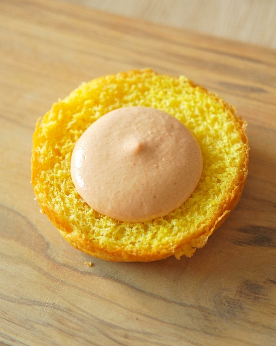 La base tostata di un panino brioche dorato con una generosa cucchiaiata di salsa arancione stesa al centro.