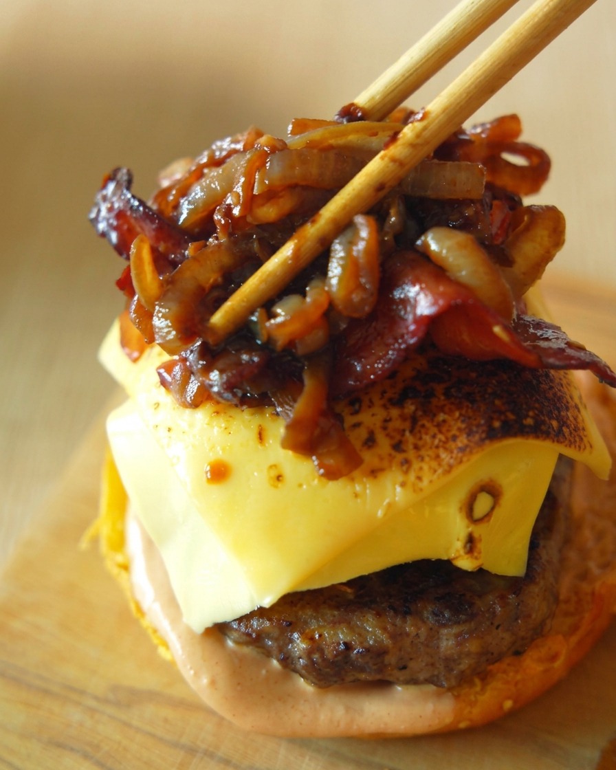Strisce di pancetta croccante e dolci cipolle caramellate posizionate con cura sopra il burger al formaggio usando delle bacchette di legno.