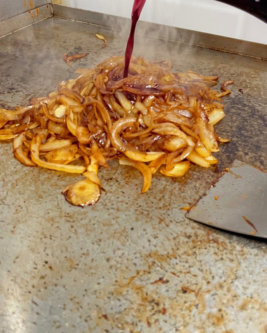 Vino rosso versato da una bottiglia su una pila di cipolle intensamente dorate su una piastra.