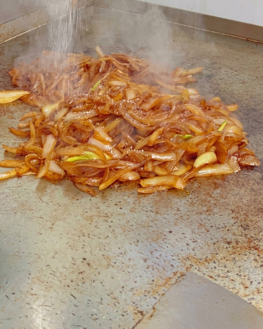 Sale fino spolverato su una pila di cipolle caramellate lucide e fumanti su una piastra calda.