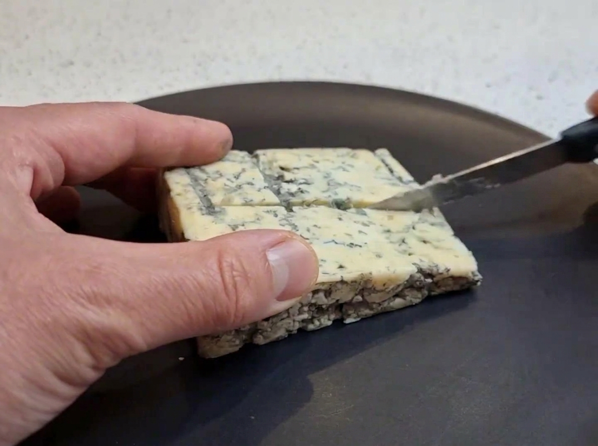 Un blocco di formaggio erborinato tagliato a cubetti su un piatto scuro.