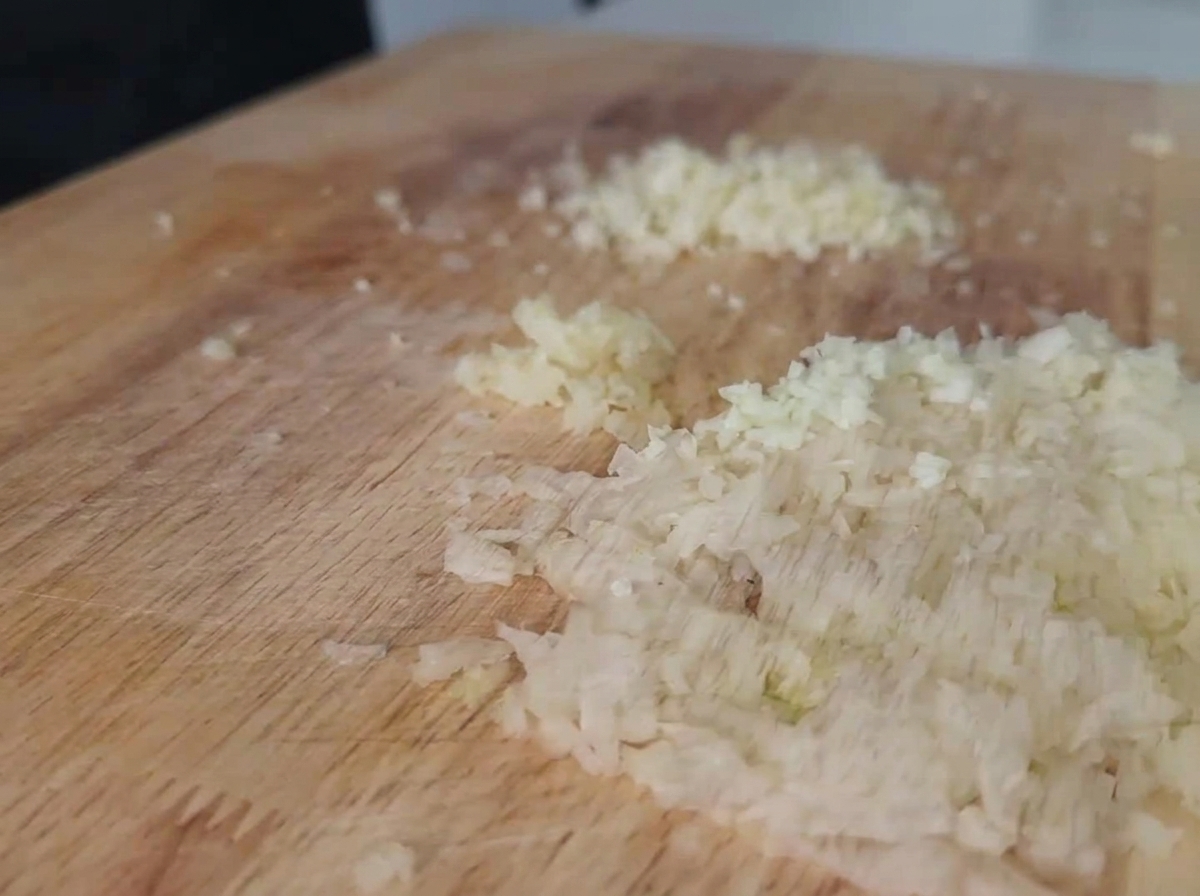 Cipolla bianca e aglio tritati finemente su un tagliere di legno chiaro.