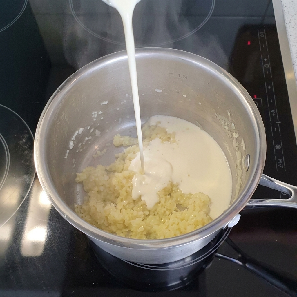 Un filo di panna liquida versato in una pentola dacciaio con cipolla e aglio soffritti.