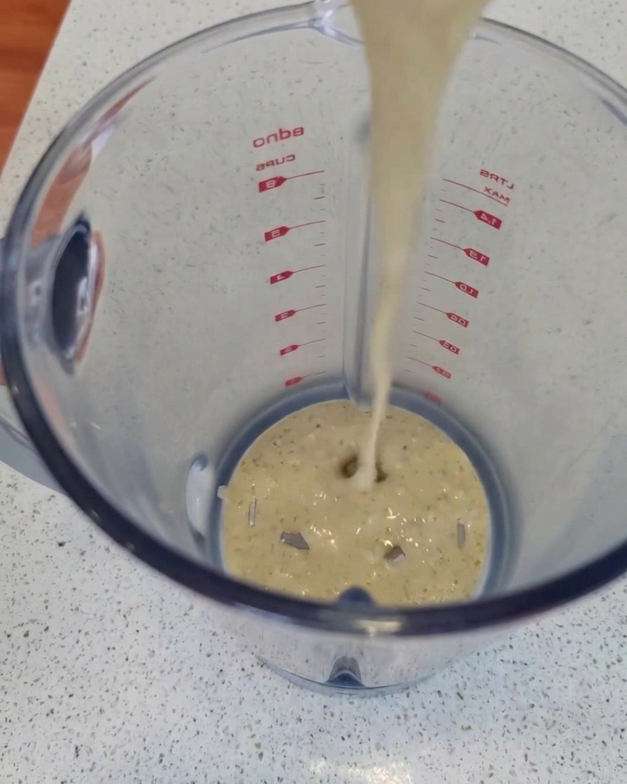 Un flusso di salsa cremosa al formaggio erborinato versato nel boccale trasparente di un frullatore.