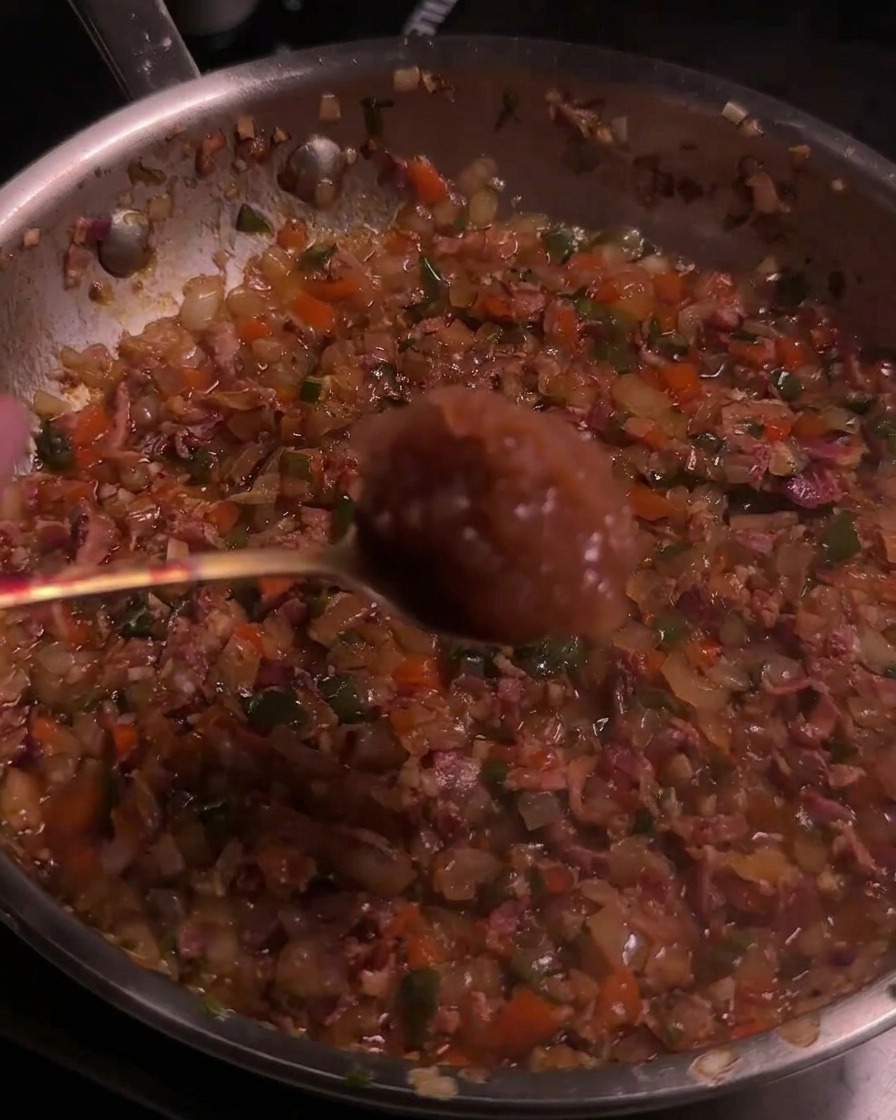 Un cucchiaio con salsa di mele viene aggiunto a un mix caramellato di bacon e peperoni in padella.