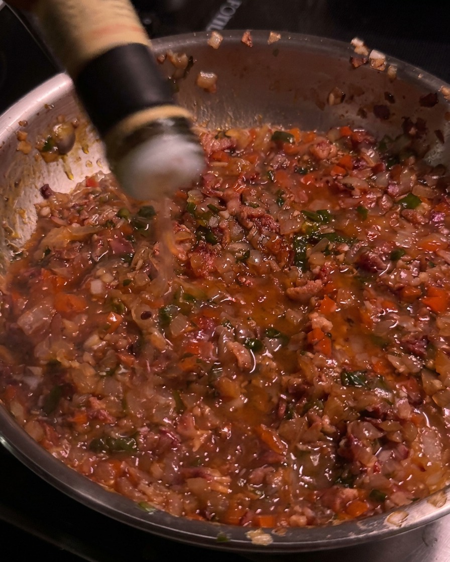 Aceto di mele versato da una bottiglia nella padella dove sobbolle la confettura di bacon.